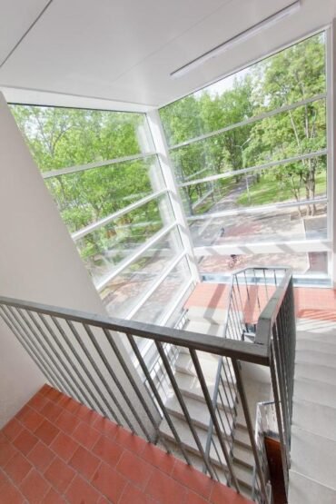 Metallpiirete ja punaste plaatidega astmetega mitmetasandilise trepi sisevaade kutsub JustResti. Suurtest akendest avaneb vaade puudega ääristatud tänavale, punastest tellistest jalutusrajale ja kauguses mööda sõitvale inimesele.