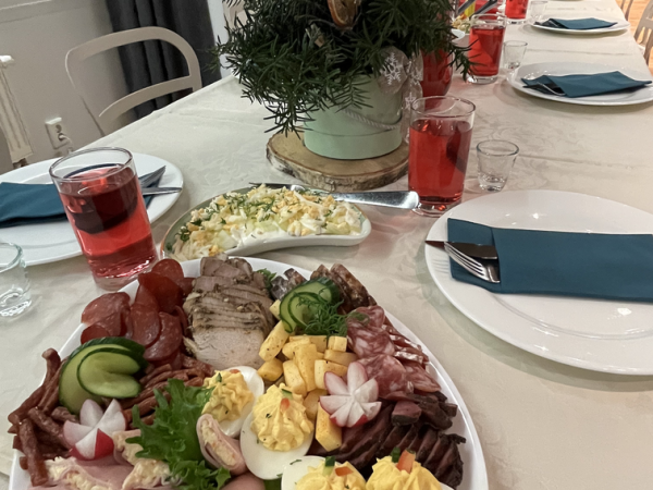 Pühadelaud, millel on vaagen erinevat liha, kuradimune ja kaunistusi. Taustal on näha salat, roosad joogid ning roheliste ja punaste kaunistustega keskosa. Elegantselt paigutatud laud on valgete ja sinakassiniste lauaseadetega.